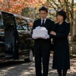 黒い礼服姿の運転手が白い風呂敷に包まれた骨壷を丁寧に抱え、遺族と共にジャンボタクシーへ乗り込む墓じまいの搬送シーン