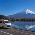 河口湖畔を走るワゴンタクシーと紅葉、雪をかぶった富士山