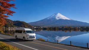 A minibus taxi driving along the shores of Lake Kawaguchi, with autumn foliage and snow-capped Mount Fuji in the background