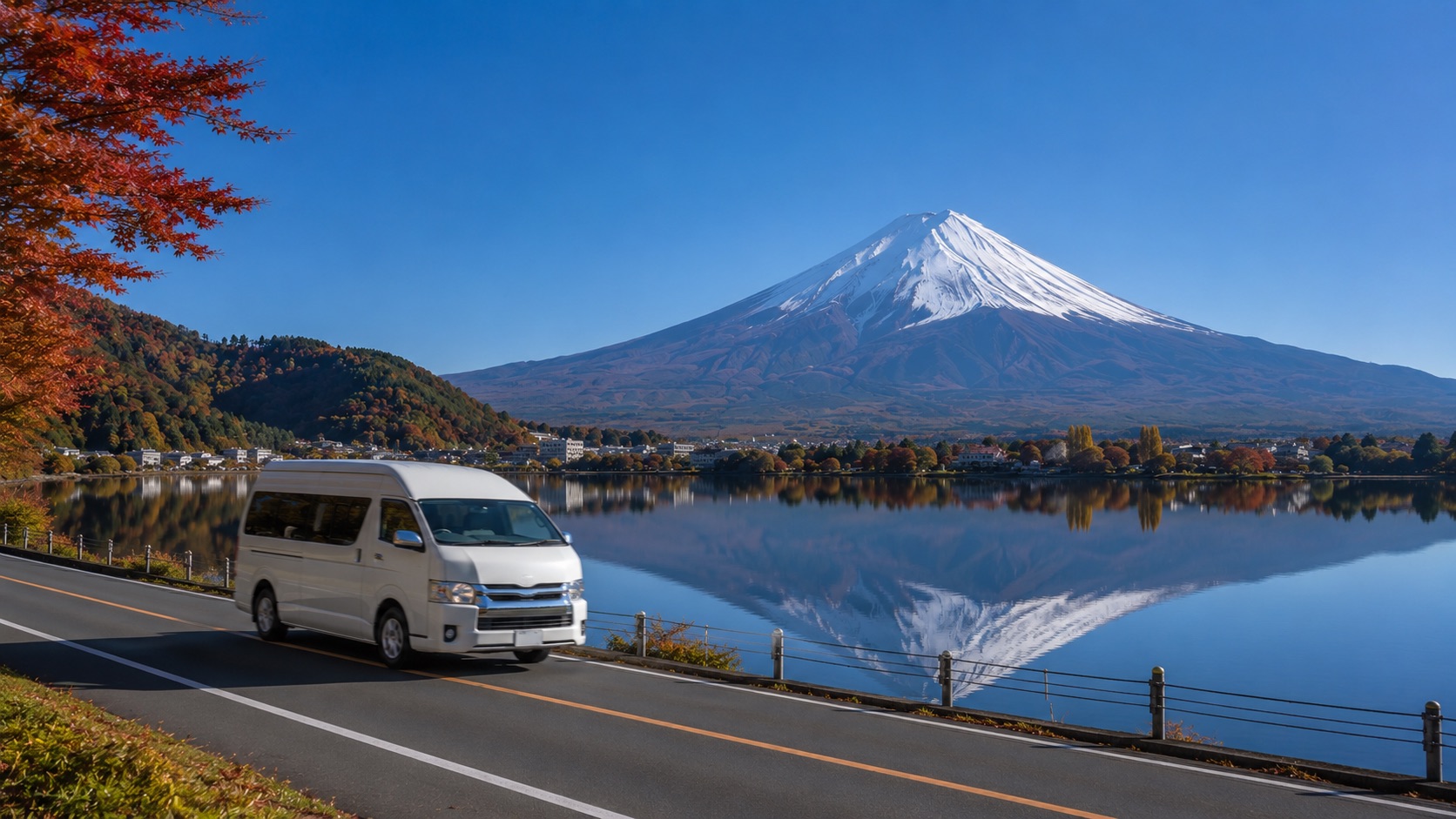 A minibus taxi driving along the shores of Lake Kawaguchi, with autumn foliage and snow-capped Mount Fuji in the background