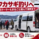 釣り道具と大型クーラーを積み込み湖畔に停まる白い大型ジャンボタクシー