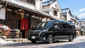 白壁と杉玉のある酒蔵の前に停まる黒いトヨタ・グランエースの貸切ジャンボタクシー