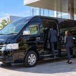 企業視察の送迎で工場前に待機する黒い貸切ジャンボタクシー（トヨタ・ハイエース ワイド スーパーロング）